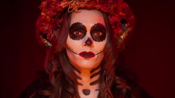 Hembra en una imagen de Halloween de una bruja con el maquillaje de un cráneo pintado, cuernos de carnero — Vídeos de Stock