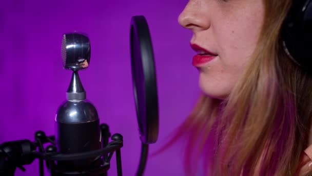 Крупный план женщины в закрытых наушниках, поющей в микрофон — стоковое видео