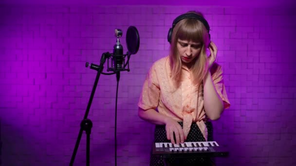 Γυναίκα μουσικός με ακουστικά στο στούντιο ηχογράφησης παίζει μια μελωδία στα πλήκτρα — Αρχείο Βίντεο