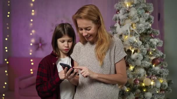 Uzun saçlı bir anne ve genç bir oğlu var. Yeni yıl arifesinde akıllı telefondan fotoğraf seçiyor. — Stok video