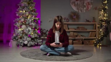 Yılbaşı arifesinde uzun saçlı sıkılmış bir adam halıya oturup telefonda sohbet ediyor.