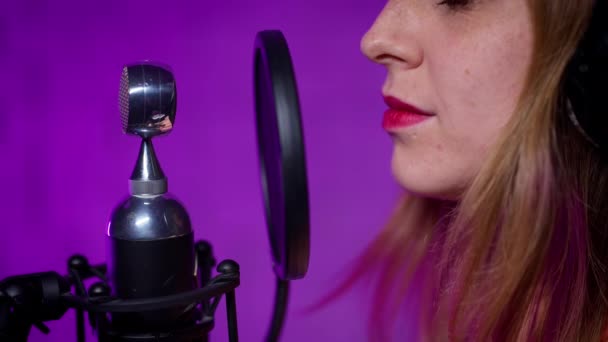 Close-upprofiel van een vrouw met een gesloten koptelefoon die in een microfoon zingt — Stockvideo