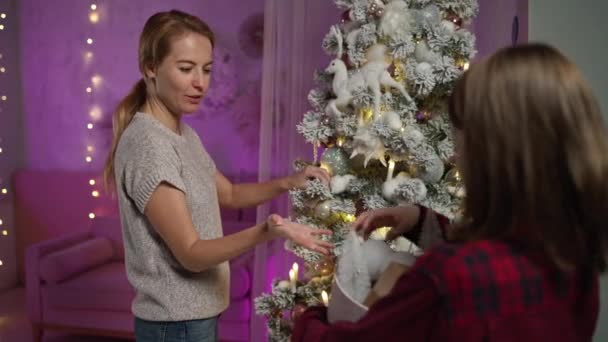 Cara de cabelos longos ajuda a mãe a decorar a árvore de Natal, dá bolas na véspera de Ano Novo — Vídeo de Stock
