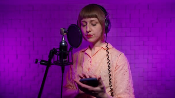 Певица в наушниках читает слова со своего телефона и поет песню — стоковое видео