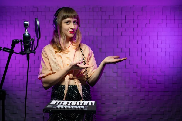 Woman singer in headphones in recording studio with microphone, synthesizer Stock Picture