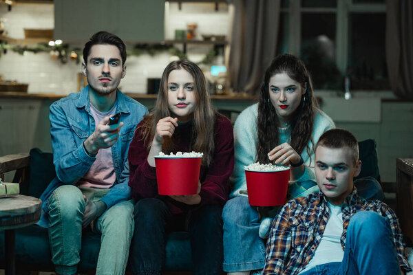 The youth company watches TV and eats popcorn with interest at a house party