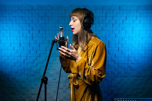 Linda cantante en auriculares canta en el micrófono en el stand en el estudio de grabación — Foto de Stock