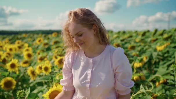 Молодая блондинка кавказская девушка на подсолнечнике в солнечный день застенчиво улыбается — стоковое видео