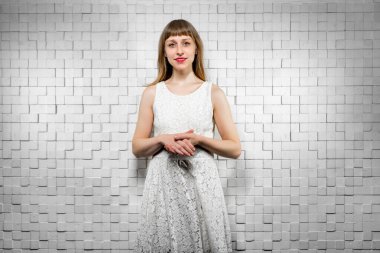 Beyaz elbiseli genç bayan utanarak kameraya bakıyor, gülümsüyor.