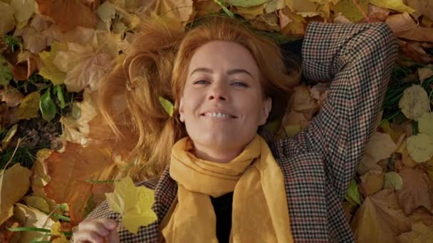 Щаслива жінка відпочиває в парку, лежить на кленовому осінньо-жовтому листі, пагони — стокове відео