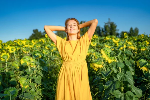 Happy free red-haired woman in yellow dress enjoys fresh air in sunflower field Stock Picture