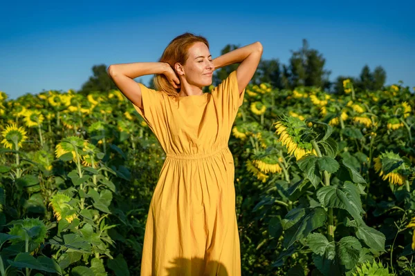 Red-haired woman in yellow dress smiling, closing her eyes in sunflower field Royalty Free Stock Images