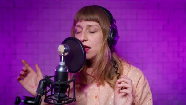 Female singer in headphones performs song into microphone in recording studio — Stock Video