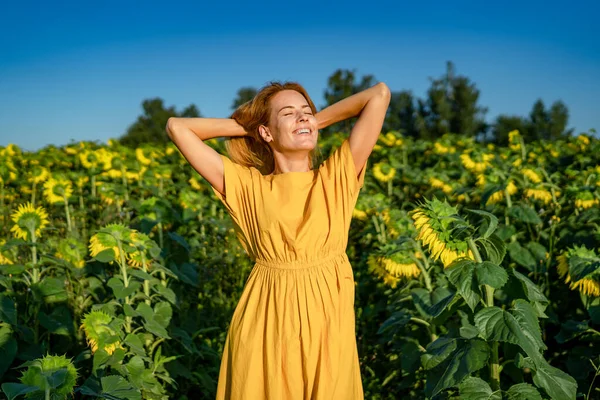 Happiness red-haired lady enjoys, smiles closing her eyes in sunflower field Stock Picture