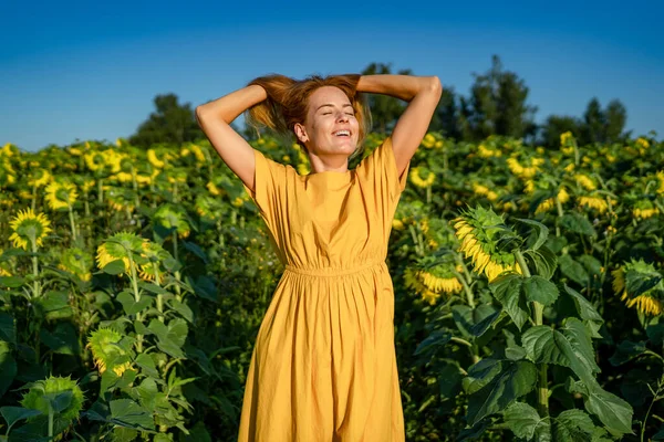 Young girl squints from sunlight, rejoices, throws hair up in sunflower field Royalty Free Stock Images