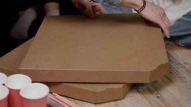 man opens cardboard box. lot of hands reach out, take apart out pizza slices