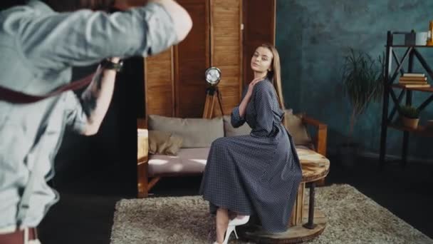 室内スタジオのテーブルに座っている写真家のための長い髪のポーズを持つモデル — ストック動画