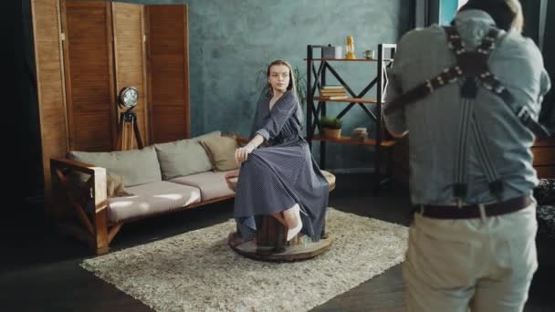Modelo com poses de cabelo longo para fotógrafo sentado na mesa no estúdio interior — Vídeo de Stock