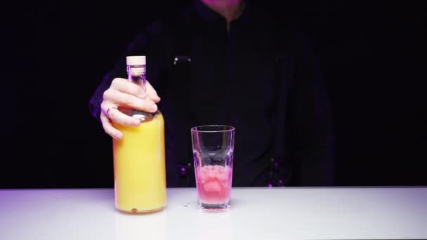 Barman nalévá pomerančový džus z láhve do sklenice s růžovým ledem — Stock video
