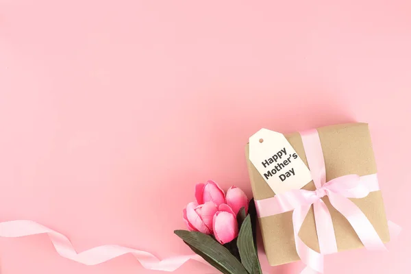 Mother\'s day background. Top view of gift box with pink bows - long ribbon , beautiful flowers and card on pastel pink background with copy space