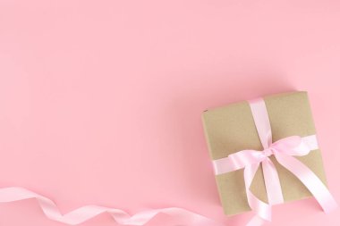 Brown paper gift box with pink satin curly ribbon bow on pastel pink background. Flat lay mother day, father day, valentines day, birthday concept with copy space.