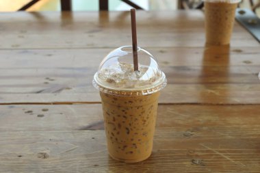 Ahşap masalarda plastik bardakta samanla buzlu kahve.