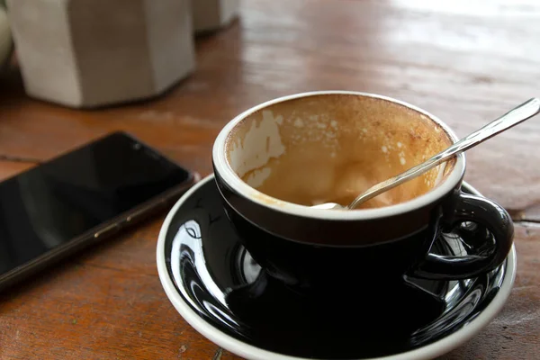 Akıllı telefon ve boş kahve fincanı ahşap masada..