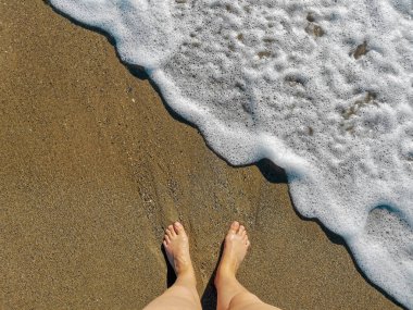 Kumlu sahilde çıplak ayaklar ve deniz köpüğü