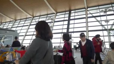 HONG KONG - 20 HAZİRAN 2020: Bavullu kadın havaalanındaki yolcu salonundaki insanların yanından geçiyor