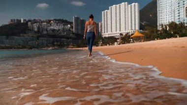 Güzel melez genç sporcu kadın gün ışığında Hong Kong sahilinde yürüyor.