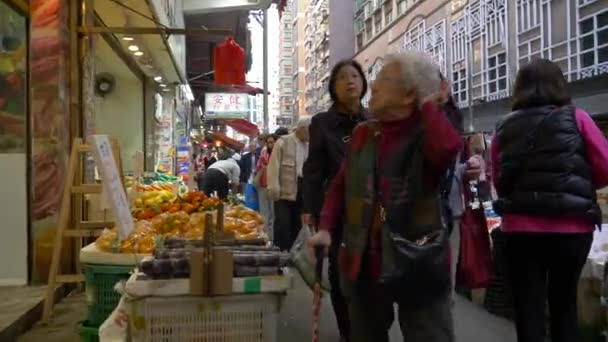 HONG KONG - JANEIRO 21, 2020: As pessoas passam por balcões e compram legumes e frutas no mercado de alimentos na China Gráficos De Vetor