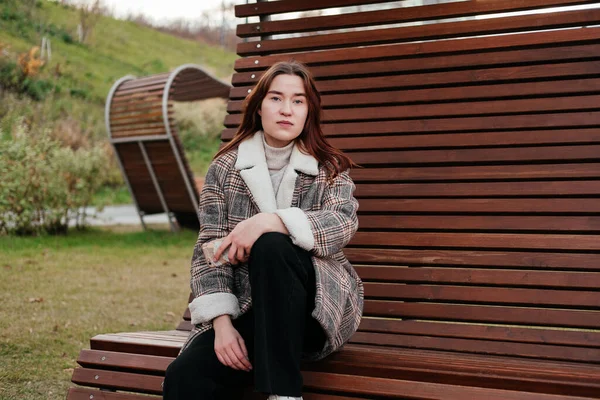 Pensive, thoughtful young woman in coat sitting alone on wooden bench. Sad woman daydreaming, thinking in autumn park. Autumn blues, feeling down. Waiting for someone. Urban casual outfit. Lifestyle — Stock Photo, Image