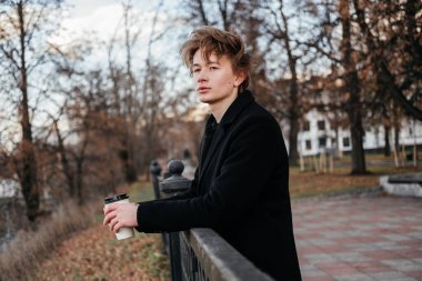 Siyah paltolu bir gencin elinde bir fincan kahveyle şehrin sokaklarında çitlere yaslanıp başka tarafa baktığını düşün. Birini bekleyen yakışıklı bir adam. Sonbahar parkında temiz hava soluyorum..