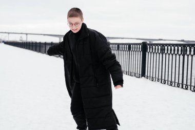 Gözlüklü, kısa saçlı, siyah düğmesiz ceketli, havanın tadını çıkaran ve kış caddesinde eğlenen genç bir kadın. Samimi insanlar. Günlük kıyafetli beyaz kadın..