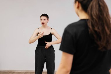 Genç konuşmacı kadın halka ders veriyor. Bayan aktör bir grup öğrenciye danışmanlık yapıyor. Manzaralı konuşma egzersizi. 20 yaşındaki koç sahnede. Kısa saçlı, siyah bluzlu ve pantolonlu kadın.