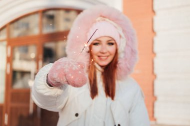Kış kenti caddesinde elinde maytapla gülümseyen kızıl saçlı kadın. 20 yaşında ceketli kızıl kız Bengal ışığına odaklan.
