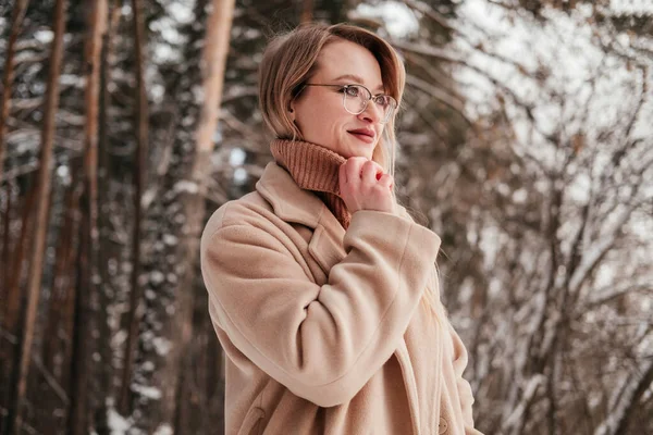 Blonde mid age woman standing in winter forest looking away to the right. Woman in coat and sweater outdoors. Girl in eyeglasses — Stock Photo, Image