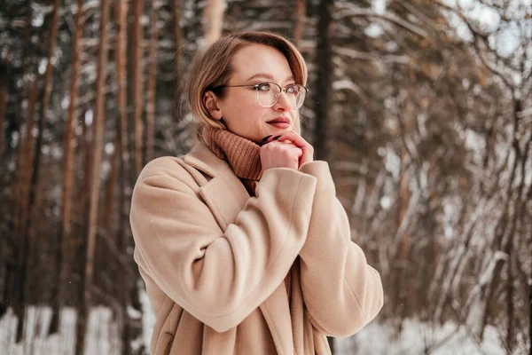 Frozen mid age woman in coat and sweater dreaming in winter forest and warming up hands outdoors. Blonde girl in eyeglasses — Stock Photo, Image