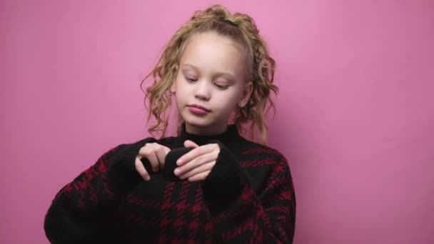 Blonde little girl in sweater puts on headphones on pink background. Kid listening music lifestyle. — Wideo stockowe
