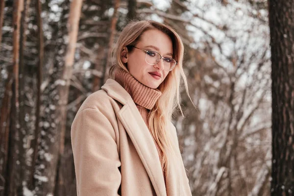 Mid age woman in finter forest looking at camera. Blonde girl in coat eyeglasses and sweater outdoors — Stock Photo, Image