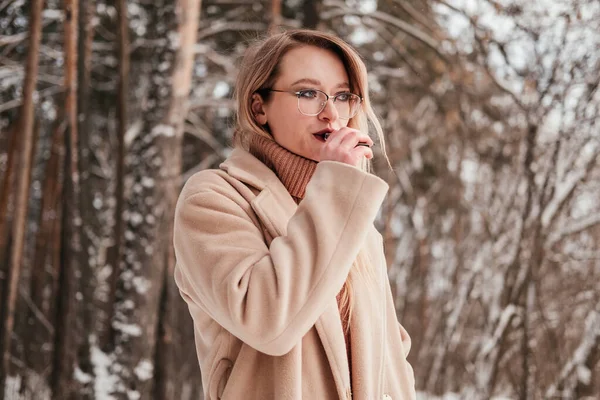 Mulher loira de meia idade fumando vape na floresta de inverno. Menina de camisola e casaco soprando fumaça ao ar livre. Conceito de saúde — Fotografia de Stock