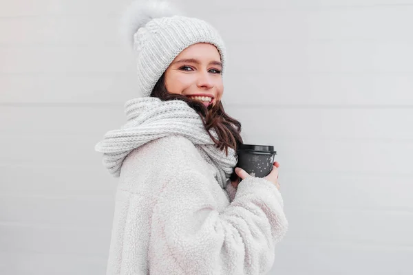 Smiling young woman in warm coat holding cup of coffee outdoors. Woman cofee lover — Stock Photo, Image