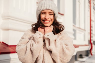 Beyaz tenli, gülen genç bir kadın. Açık bir şehir caddesinde duruyor.