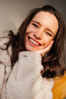 Kapalı alanda kameraya bakan esmer kıvırcık saçlı, gülümseyen genç kadının portresini yakından çek.