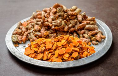 Zerdeçal (Curcuma longa) yakın çekim, taze dilimlenmiş zerdeçal ve kökler bir tabakta birikir.