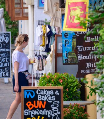 Galle, Sri Lanka - 02 03 2022: Galle Kalesi sokaklarından alışveriş yapan beyaz kız, renkli tahtalar, tekstil ve hediyelik eşya dükkanları.