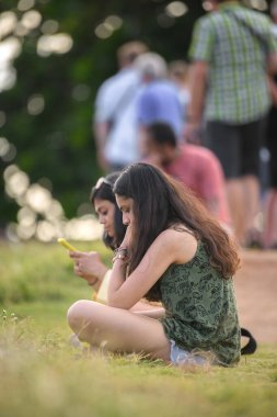 Galle, Sri Lanka - 03 31 2022: Otların üzerinde oturan ve cep telefonlarına bakıp özgürlüğün tadını çıkaran güzel kızlar.