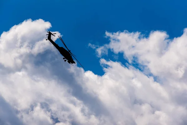 Silhouette of military attack helicopter in flight against blue sky and white clouds
