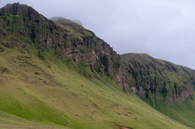 Vik İzlanda yakınlarındaki çimenli dağ uçurumunun bulutlu manzarası