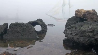 zeilboot in volledige zeil komt uit mist